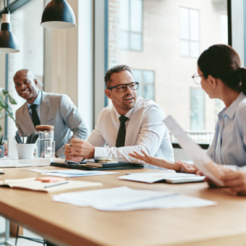 Diverse group of coworkers in a modern office discussing documents around a wooden conference table.