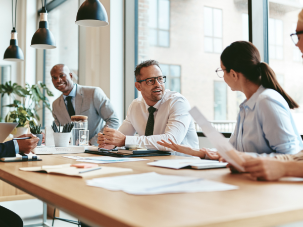 Why-Executive-Leaders-Must-Align-with-HR-And-How-It-Drives-Business-Success - Career Image Solutions Diverse group of coworkers in a modern office discussing documents around a wooden conference table.